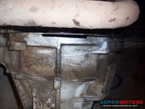 Close-up of a dirty transmission housing with an exhaust pipe above it