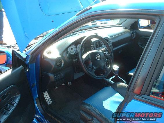 Blue car interior with black dashboard, steering wheel, and seats with blue accents. Hood is open