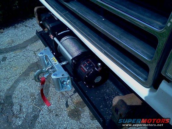 Winch mounted on vehicle bumper with tow hook and red strap