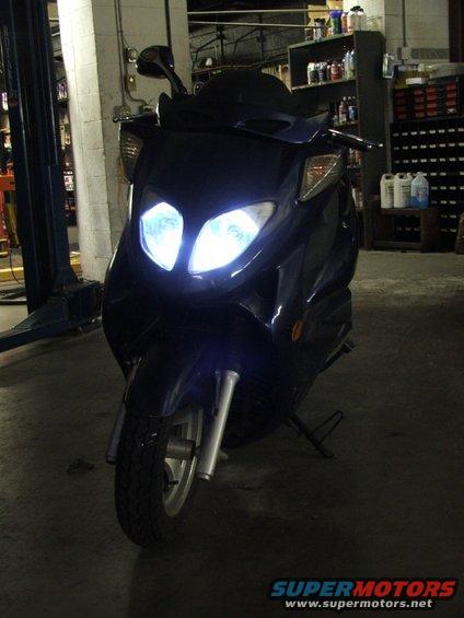 Dark blue scooter with bright headlights, parked indoors