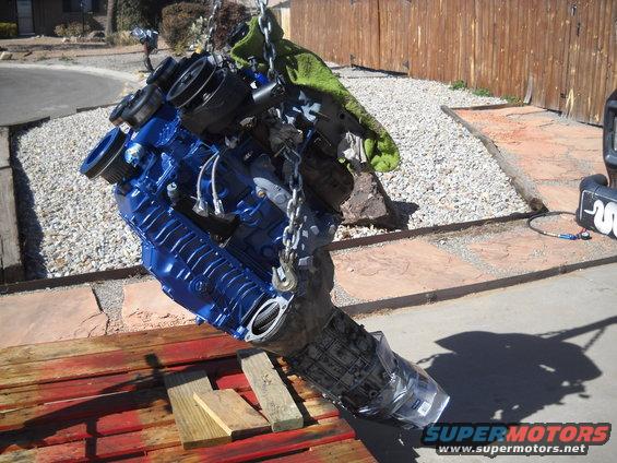 engine and transmission assembly hanging from a chain, painted blue