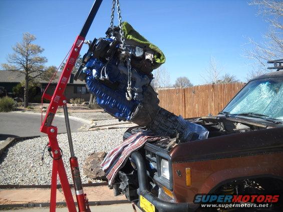 Brown SUV with engine being removed by a red engine hoist