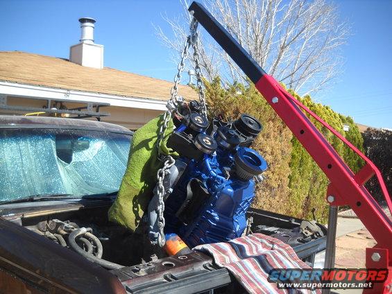 Engine being lifted by a red engine hoist out of an open hood. A green blanket is draped over part of the engine