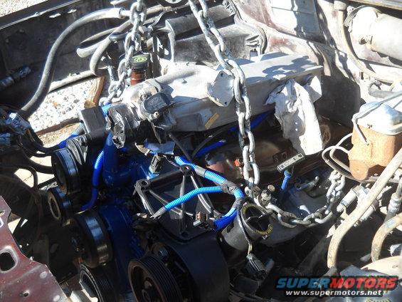 Engine with blue hoses and chains, being lifted