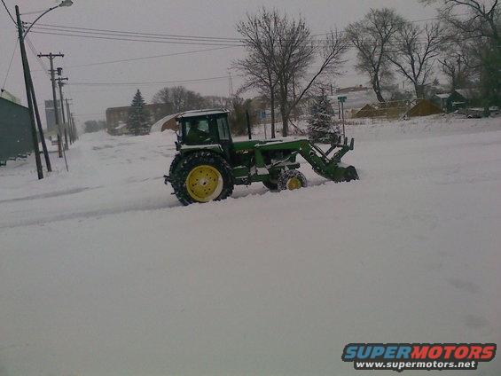 Tractor with front loader plowing snow on a street