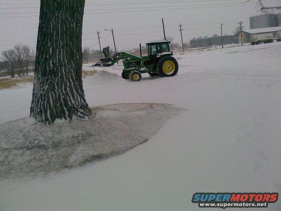 Tractor with front loader in a snowy field next to a large tree