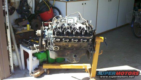 Engine on yellow stand in garage. Supermotors.net logo visible