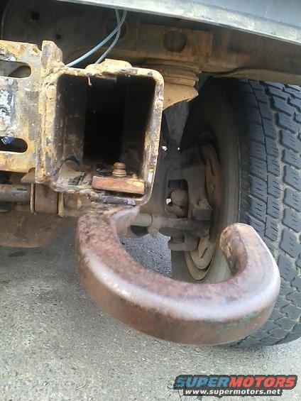 rusty tow hook attached to a vehicle's frame, with a tire visible to the right