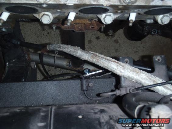 Close-up of engine block with spark plugs and exhaust pipe. Supermotors.net logo visible