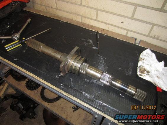 Transmission input shaft with splines on both ends, resting on a workbench with tools