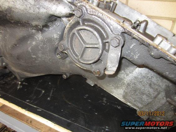Close-up of a metal transmission component with a circular cover secured by bolts