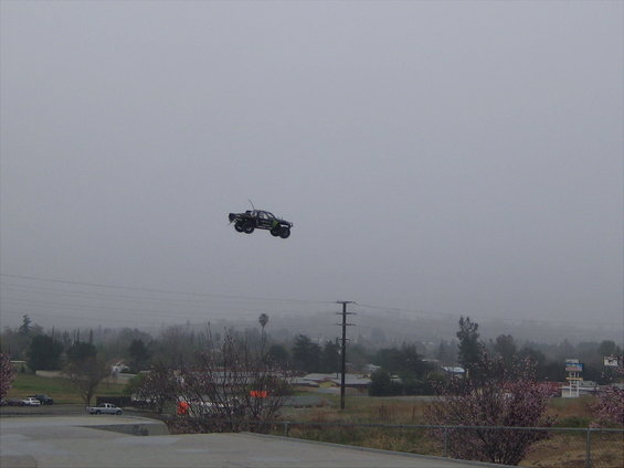 RC monster truck airborne against a hazy sky, with a suburban landscape below