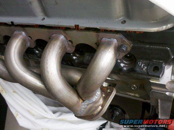 Close-up of a newly welded exhaust manifold attached to a black engine block