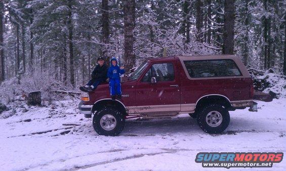 Maroon Ford Bronco with tan top parked in snow, two children on hood