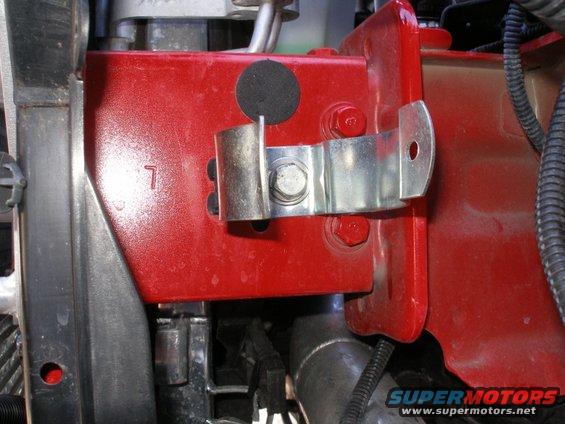 Red painted metal bracket with a clamp bolted to it, part of a vehicle's engine bay