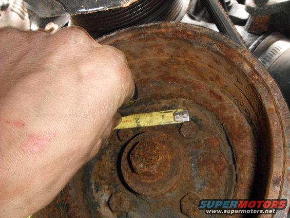 hand holding tape measure against rusty pulley