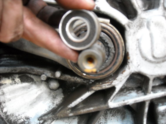 Hand holding a bearing over a worn shaft assembly with grease and dirt