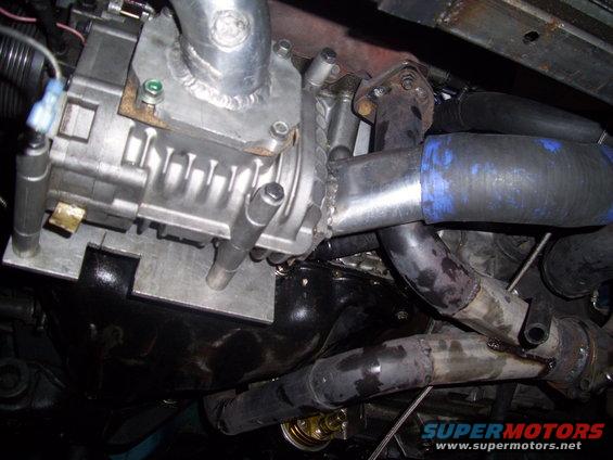 Close-up of a supercharger bolted to an engine, with various pipes and hoses connected