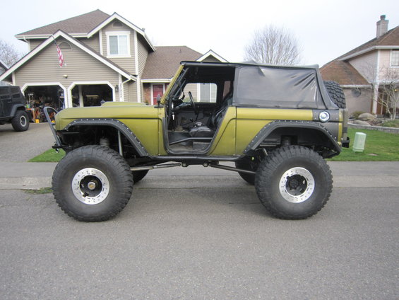 Olive green Ford Bronco with large off-road tires and a soft top, parked in a driveway