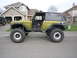 1974 Ford Bronco - A heavily modified Ford Bronco sits parked in front of a suburban house, showing off its lifted suspension and oversized wheels.