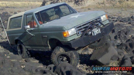 Green Ford Bronco with a white star on the hood, off-roading over rocks