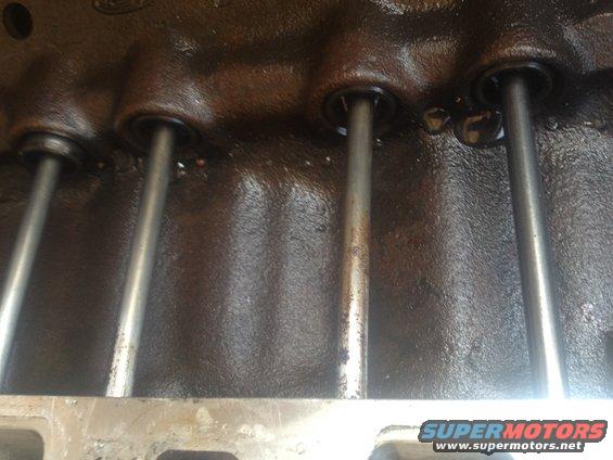 Engine block with pushrods visible, dark oily surface, part of a motor rebuild