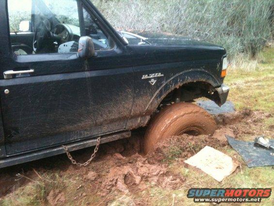 Black truck stuck in mud, front wheel deep in dirt. Side view shows door and fender
