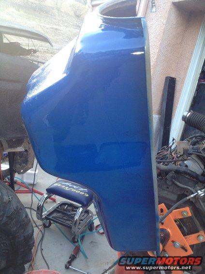 blue fender section of a vehicle, possibly undergoing repair or restoration. Tools and engine parts are visible in the background