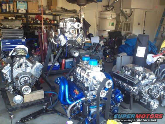 Three custom V8 engines with chrome and blue accents in a garage setting. One engine is on a stand