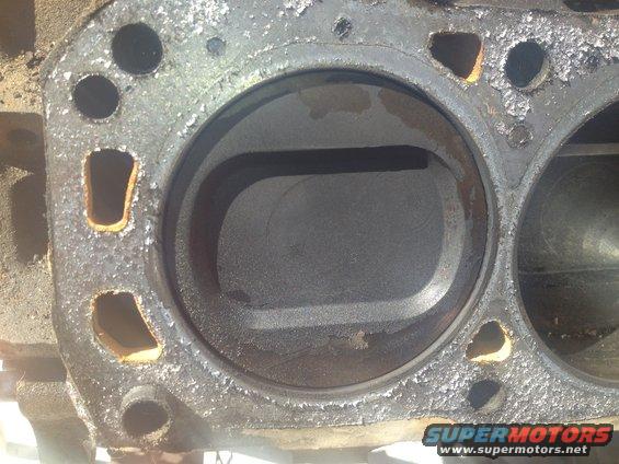 Close-up of an engine cylinder block with two cylinders visible. The surface is dirty and shows signs of wear