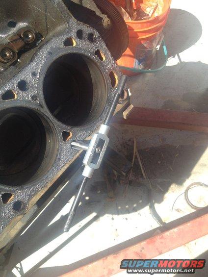 Engine block with cylinders and a tap tool inserted into a bolt hole