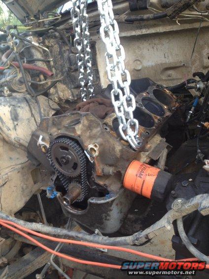 Engine block with timing chain and gears, orange oil filter, and lifting chains. Dirty and disassembled