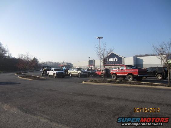 Several trucks and SUVs parked in a lot in front of a Lowe's store. A red 1979 Ford Bronco is prominently featured