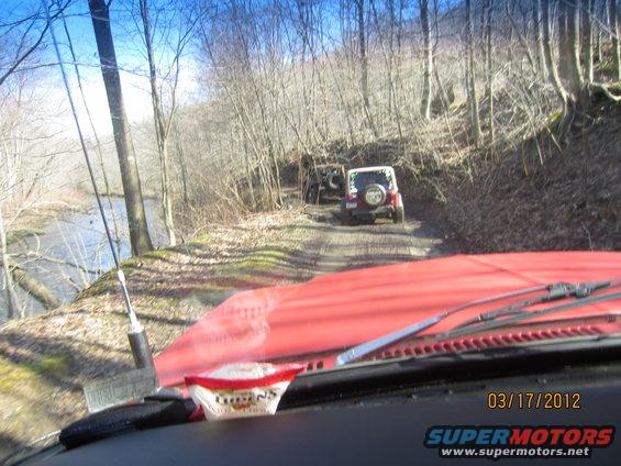 Interior view of red vehicle, two Jeeps on dirt road by river in woods