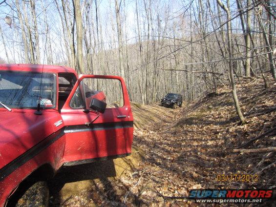 1979 Ford Bronco and black SUV on wooded trail. Red Bronco door is open