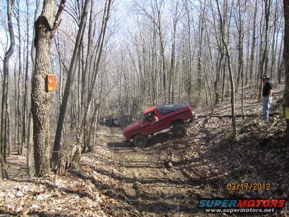 Red 1978 Ford Bronco off-roading on a muddy trail in a forest