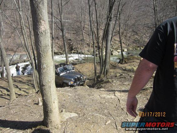 Jeep Wrangler navigating a steep, wooded trail next to a fast-flowing river. Date stamp reads 03/17/2012