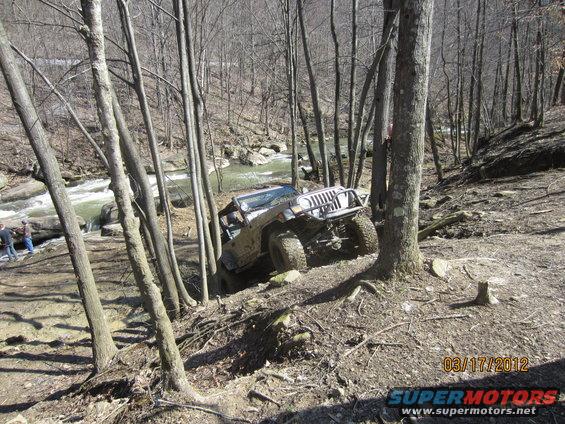 Jeep Wrangler navigating a steep, wooded trail next to a river