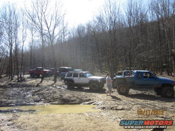 Off-road vehicles gathered in a muddy, wooded area