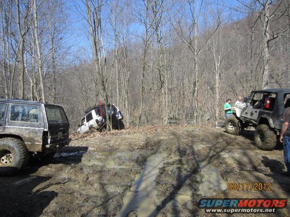 Jeep stuck in mud, another Jeep and SUV nearby in wooded area