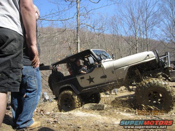Jeep Wrangler with large tires climbing a muddy incline, two people watching