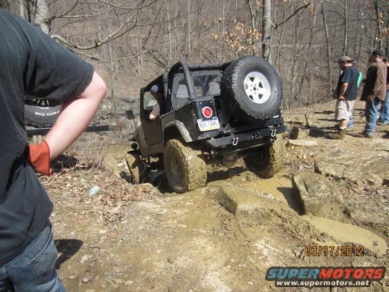 Jeep Wrangler navigating a muddy, rocky trail with people watching