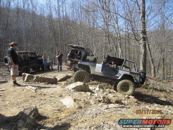 Off-road vehicles navigating a rocky trail with trees in the background