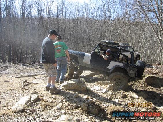 Jeep on rocky trail with two people watching. Another SUV is behind it