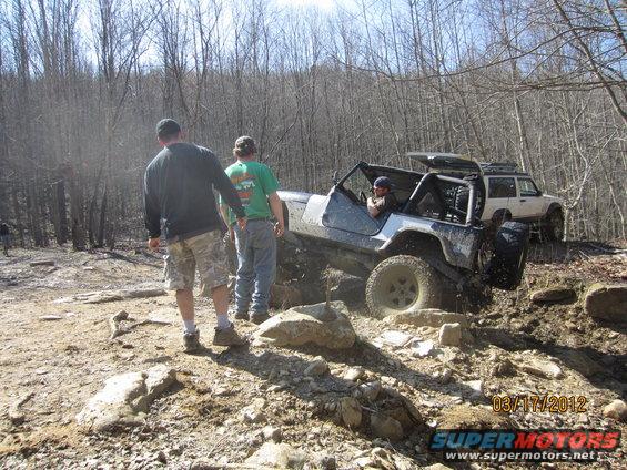 Two off-road vehicles navigating a rocky trail with trees in the background