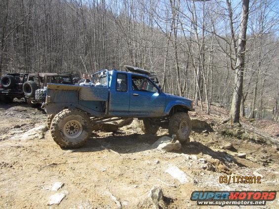 Blue off-road pickup truck with large tires navigating a rocky trail