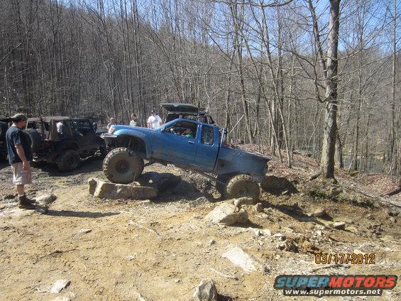 Blue pickup truck with large tires navigating rocks on a dirt trail