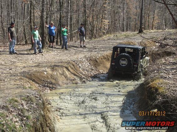 Jeep Wrangler navigating a muddy off-road trail with spectators watching