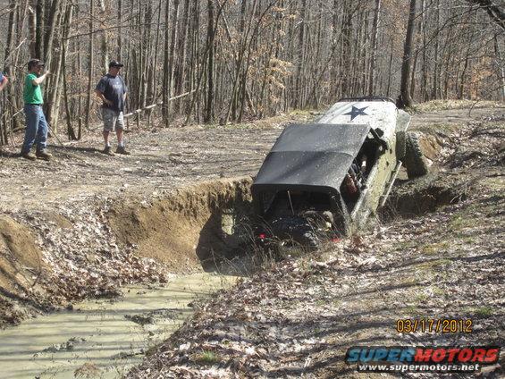 Off-road vehicle navigating a muddy ditch with people watching