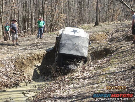 Off-road vehicle tilted in a muddy ditch, with a star emblem on its hood